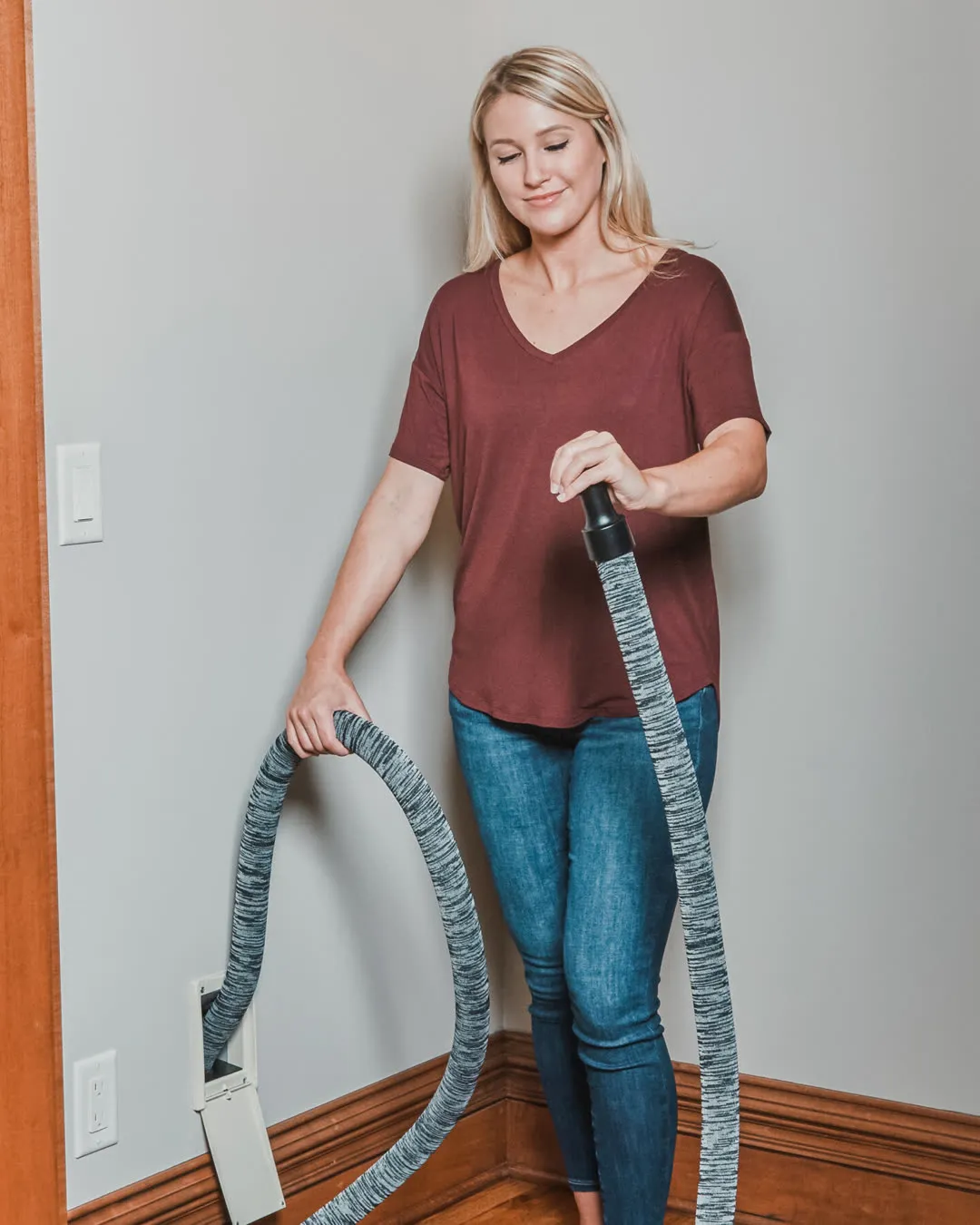 Homeowner cleaning with a central vacuum hose plugged into a wall inlet